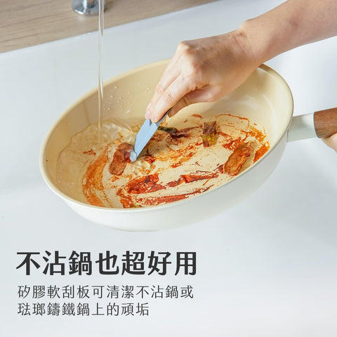 家庭主婦在廚房輕鬆使用魔刮多功能清潔刮板清理不沾鍋,顯示矽膠部分有效去除鍋面污漬而不損傷表面。